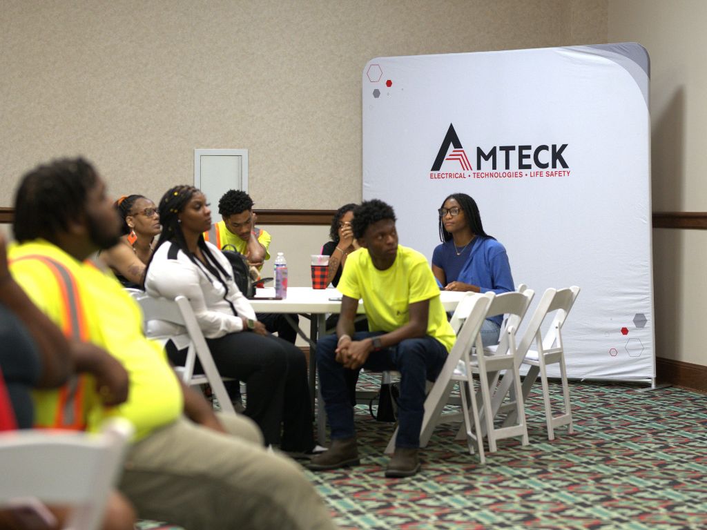 People sit at a table in front of a backdrop that says Amteck