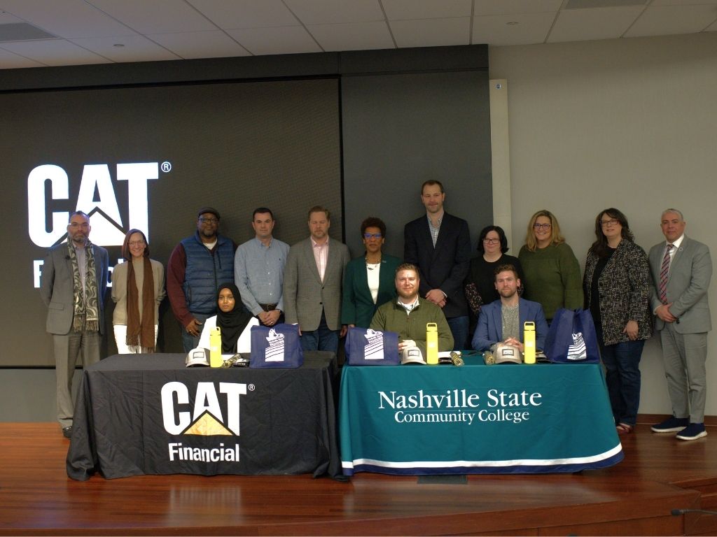 A group of people stand at or behind two tables, with one tablecloth reading CAT Financial and the other reading Nashville State Community College