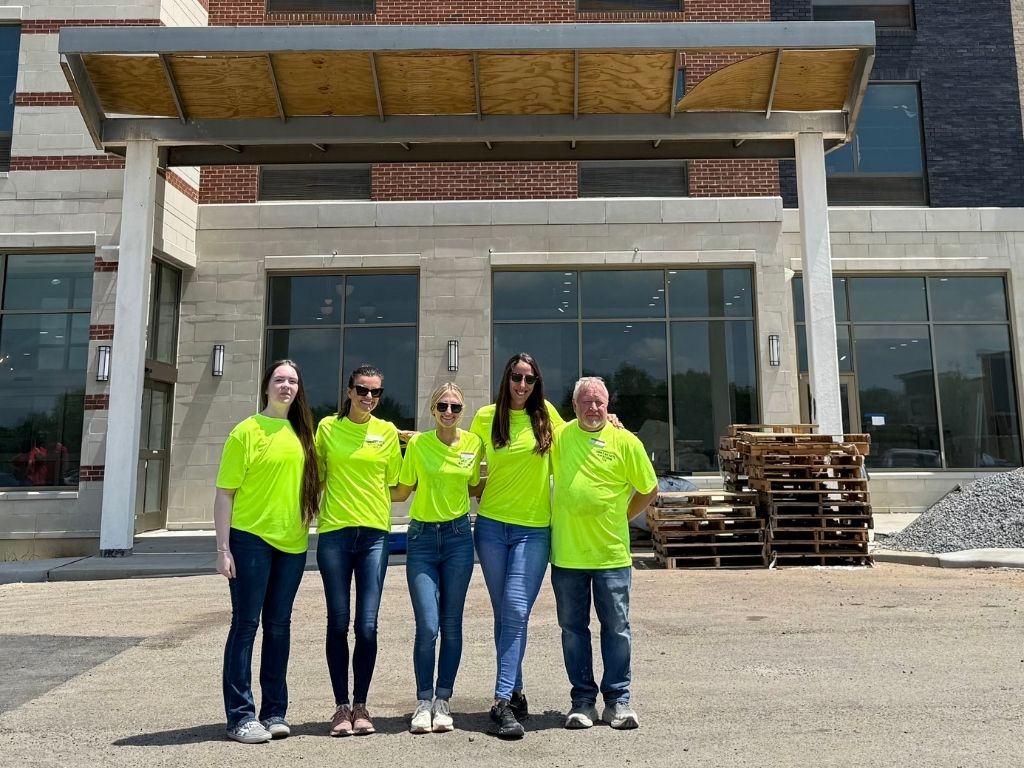 Five people pose for a photo in front of a TownPlace Suites hotel
